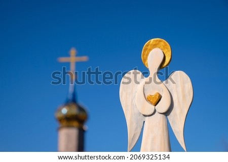 Wooden figure of an angel with a golden heart in his hands on a church and blue sky background.
