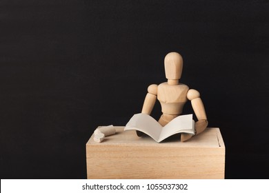 Wooden figure is reading a book while sitting at workplace against black background, copy space. Reading, education concept. - Powered by Shutterstock