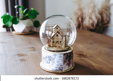 Wooden figured snow globe. Home decoration objects on the wooden table. Big snow globe with wooden house inside.