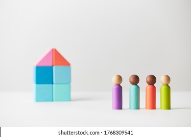 Wooden Figures Concept. Four People Standing In Front Of A Large Multi Generations House, Mixed Race Skin Colour, Four Adults. Realty Market.