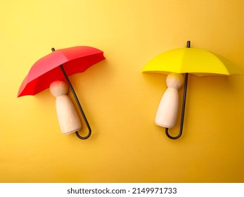 Wooden Figures Covered By Umbrella On A Yellow Background. Personal Insurance Concept.