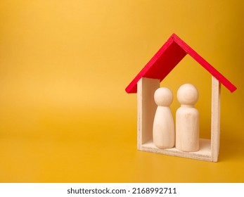 Wooden Figures Husband And Wife Inside Wooden House On A Yellow Background With Copy Space.