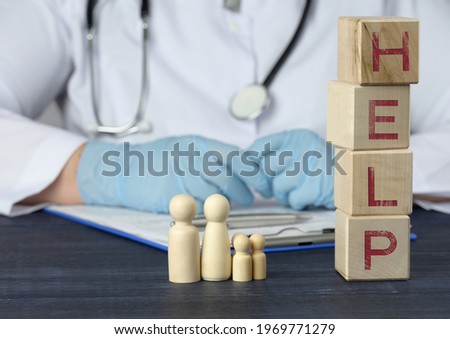 wooden figures of men and the inscription help on wooden cubes, behind the table sits a medic. Medical care concept, insurance, trust