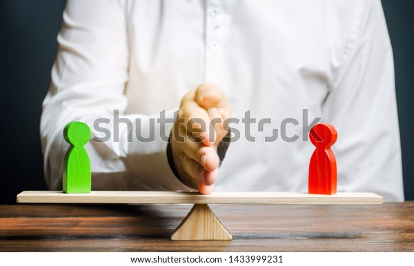 Wooden figures of people on scales and a\
mediator / arbitrator. Resolving conflict situations and disputes.\
Conclusions of the peaceful resolution of disputes. Conflict of\
interest. Business\
opponents