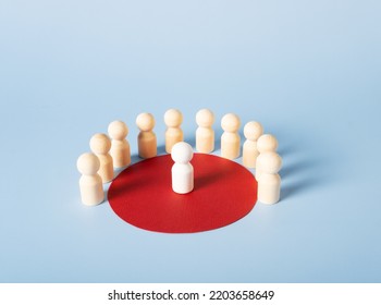 Wooden figures of people stand in a red circle, in the center of which is one white figure. The concept of a group, a society, a meeting. - Shutterstock ID 2203658649