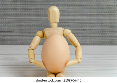 wooden figurine of a man holding a chicken egg in his hands. Wooden mannequin with an egg. Creative image. Easter preparation concept, agriculture support, proper nutrition, idea. Space for text