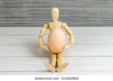 wooden figurine of a man holding a chicken egg in his hands. Wooden mannequin with an egg. Creative image. Easter preparation concept, agriculture support, proper nutrition, idea. Space for text