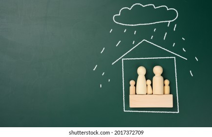 Wooden Figurines Of A Family In A House Drawn With White Chalk And Rain From A Cloud. Real Estate And Family Insurance Concept. Natural Disaster Protection, Copy Space