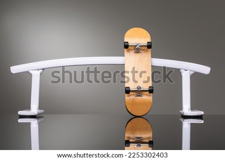 Wooden fingerboard and white metal railing on a gray gradient background, a small skateboard