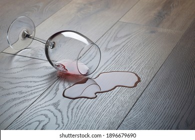 Wooden floor with overturned glass of red wine. Spilled wine on a wooden laminate (parquet) floor with moisture protection. Concept of alcoholism, broken relationships, depression