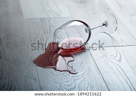 Wooden floor with overturned glass of red wine. Spilled wine on a wooden laminate (parquet) floor with moisture protection. Concept of alcoholism, broken relationships, depression