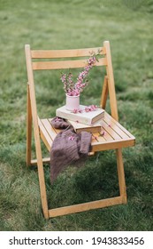 Wooden Folding Chair, Stands On The Green Grass. There Is A Stack Of Thick Books In A Light Cover. At The Top Is A Pink Vase With Pink Almond Blossoms. Spring Bloom. Reading Books In The Park. Spring.