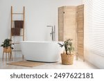 Wooden folding screen, bathtub and green houseplants in bathroom