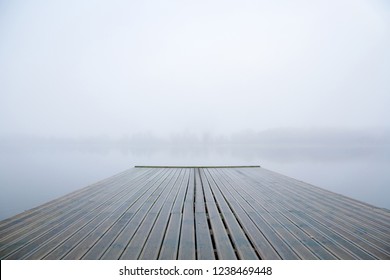 Wooden footbridge on lake. Mist over water. Foggy air. Early chilly morning in late autumn. Peaceful atmosphere in nature. Empty place for text, quote or sayings.
