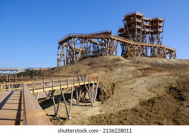 Wooden Footbridge With Silhouettes Of Walking People And Wooden Lookout Tower At Kurza Gora In Background. Kurzetnik, Warmia And Masuria, Poland