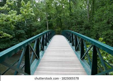 Wooden Footpath Bridge With Metal Handrails Crossing Creek Through Forest Perspective