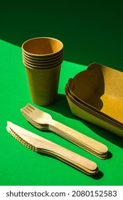 Wooden Forks And Paper Cups With Plates On Green Background. Eco Friendly Disposable Tableware. Used In Fast Food, Restaurants, Takeaways, Picnics. No Plastic Zero Waste