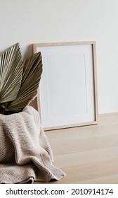 Wooden Frame Mockup On Beige Table, Beige Knitting Plaid And Dry Palm Leaves.White Wall Background. Scandinavian Interior. Copy Space.