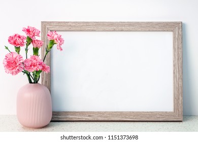 Wooden frame mockup with a pink notched vase with carnations on a desk with the terrazzo pattern - Shutterstock ID 1151373698