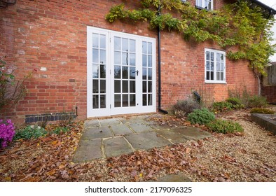 Wooden French Doors And A York Stone Patio In A UK Landscaped Garden With Autumn Leaves