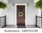 A wooden front door detail with grey vinyl siding, composite decking floor and raining, and lights mounted aside the doorway.