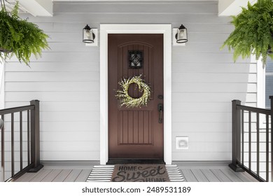 A wooden front door detail with grey vinyl siding, composite decking floor and raining, and lights mounted aside the doorway.