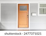 A wooden front door with a glass window on a grey and white homes covered front porch.