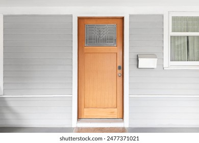 A wooden front door with a glass window on a grey and white homes covered front porch.