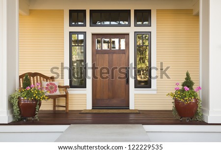 Wooden front door of a home. Front view of a wooden front door on a yellow house with reflections in the window and a wide view of the porch and front walkway. Horizontal shot.