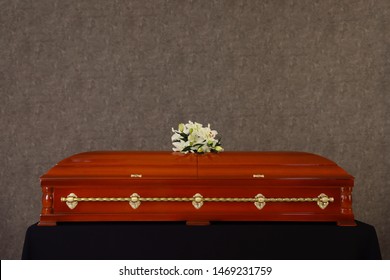 Wooden Funeral Casket With White Lilies At Grey Wall