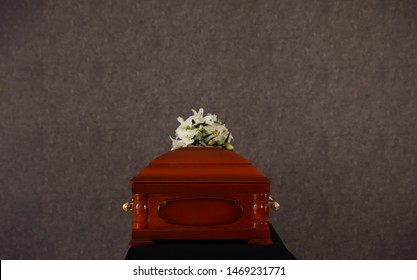 Wooden Funeral Casket With White Lilies At Grey Wall