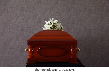 Wooden Funeral Casket With White Lilies At Grey Wall