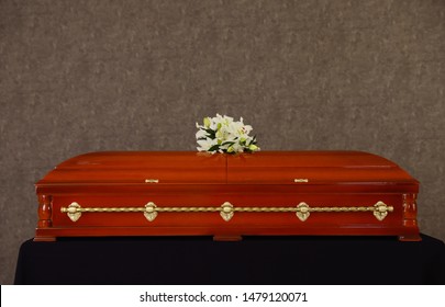 Wooden Funeral Casket With White Lilies At Grey Wall