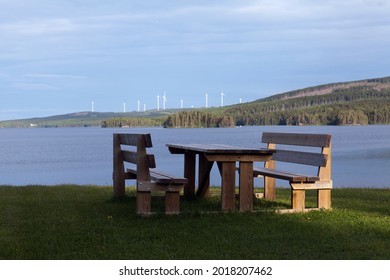 Wooden Furniture Group On A Hill This Side A Lake. Ridges And Wind Turbines In The Background.