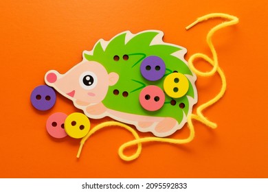 Wooden game lacing hedgehog. Wooden hedgehog, wooden buttons and lace on an orange background. Montessori toys, the development of fine motor skills, logic, the study of colors.