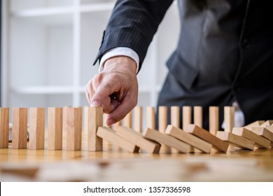 Wooden game strategy, Businessman hand stopping falling wooden dominoes effect from continuous toppled or risk, strategy and successful intervention concept for business. - Shutterstock ID 1357336598