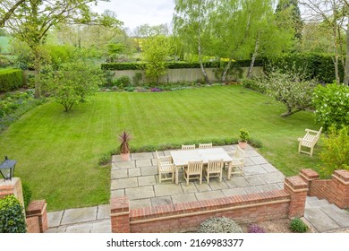 Wooden garden furniture on a patio terrace in a UK landscaped back garden with large lawn