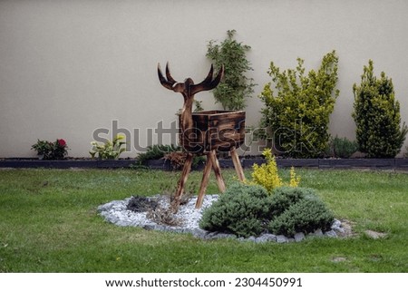 Wooden garden sculpture of a deer - against the background of flowers and a wall. Wood fired decoration.