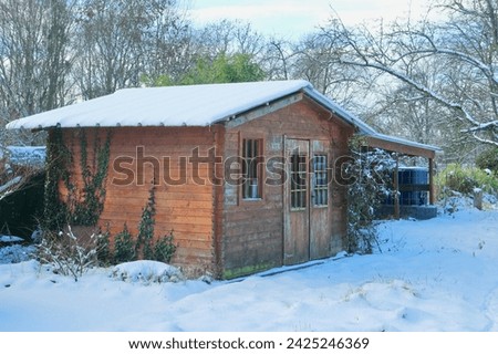 Wooden garden shed on a lawn, covered in snow.