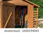 A wooden garden shed standing on a concrete foundation in a garden, visible garden tools.