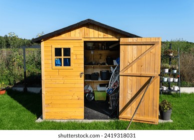 A wooden garden shed standing on a concrete foundation in a garden, flowers and tools visible.