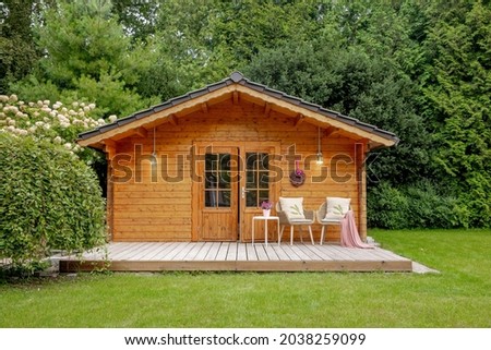 Wooden garden shed with two chairs outside. Wooden house with a large garden and a white panicle hydrangea 