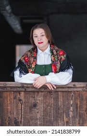 At The Wooden Gate Stands A Slavic Woman In A Rustic Headscarf. Portrait Of A Country Woman