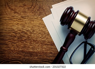 Wooden gavel with a brass band and glasses on notepaper conceptual of a judgement in law, justice or an auctioneers gavel, view from above on a wooden desk with copyspace