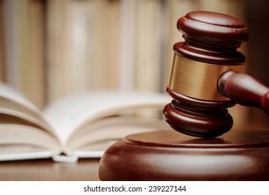 Wooden gavel resting on its end on a wooden table in front of an open law book conceptual of a judge, courtroom and judgements