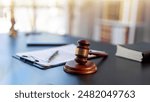 A wooden gavel sits on a desk next to a stack of books and a clipboard. The gavel is a symbol of authority and justice, and the books suggest that the desk is a workspace for a lawyer or judge