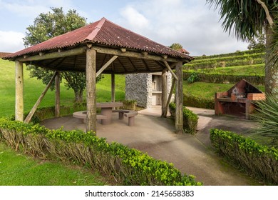 Wooden gazebo with slate roof and brick stove for cooking food outdoors. Public park with picnic table and bench in arbor, close to barbeque grill oven. Backyard with patio and open fireplace