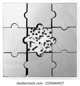  Wooden Gears Under The Puzzle, The Concept Of Moving To The Next Level. Cog Wheels Coming Out From Underneath A Jigsaw Puzzle. Solving The Problem Concept - Puzzles And Cogwheels.