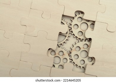 Wooden Gears Under The Puzzle, The Concept Of Moving To The Next Level. Cog Wheels Coming Out From Underneath A Jigsaw Puzzle. Solving The Problem Concept - Puzzles And Cogwheels.