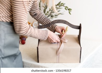 Wooden Gift Box In Female Hands With Spring Flowers On Light Natural Fabric Background. Easter Basket With Traditional Food For Serving Holiday Table.